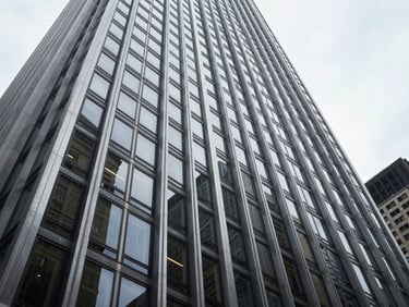 Low-angle architectural crop of a modernist steel and glass skyscraper facade in Midtown Manhattan, sharp overcast daylight, deep shadows, clean geometric lines.
