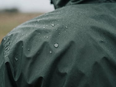 Macro close-up texture of dark green technical waterproof fabric with rain droplets, moody overcast daylight, desaturated tones