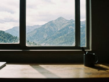 Moody film photography of a remote workspace with a view of overcast mountain peaks through a large window, high-contrast shadows, 35mm grain