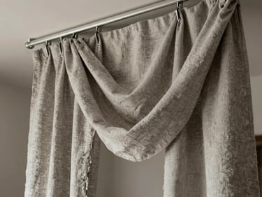 Close-up of heavy linen drapery folds hanging from a slim ceiling track in a high-ceilinged Mexico City apartment, soft north-facing daylight, neutral stone-grey fabric texture visible