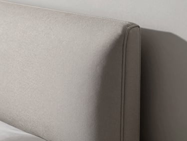 Detail of upholstered headboard in a luxury bedroom, hand-stitched seam line visible under raking north light, dove-grey fabric taut over a crisp corner, architectural precision