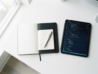 Overhead flat-lay of a minimalist white desk with a black notebook, a silver mechanical pencil, and a tablet displaying a clean code editor, bright natural light, electric blue accents.