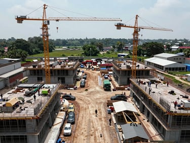 Wide environmental shot from above of two simultaneous construction sites separated by distance, crews working in both, cranes visible, natural daylight, documentary aerial framing showing scale of multi-site operations