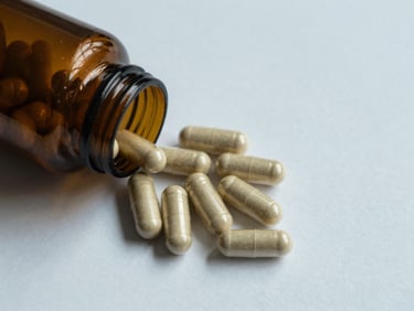 Overhead flat-lay of magnesium glycinate capsules spilled from an open amber bottle onto a white surface, cool north-facing daylight, clinical isolation framing