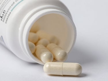Extreme close-up of a white capsule supplement bottle isolated on a clean white surface, cool even studio lighting, label texture in sharp focus, overhead perspective, clinical product photography