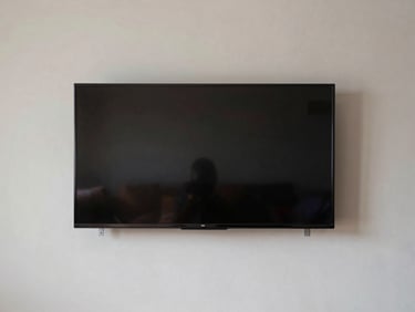 Wide shot of a flat-screen TV flush-mounted on a painted drywall, level and centered, mounting bracket hardware visible at edges, daylight-neutral interior, no people