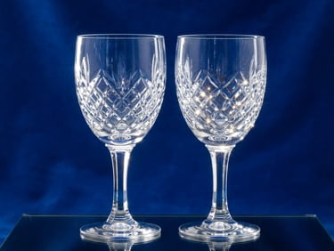 Crisp product portrait of high-clarity crystal goblets catching bright studio light, sharp reflections, clean refractions, royal blue background, professional commercial photography.