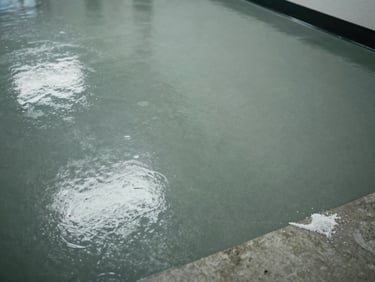 Overhead close-up of a smooth epoxy floor in a school corridor under fluorescent light, salt-stained concrete visible at edge, grey-green tint, no people