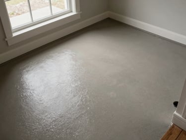 Overhead shot of a residential entryway epoxy floor, warm grey tone, natural daylight from side window, no people, surface detail and edge transition visible
