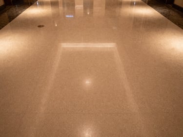 Wide overhead shot of hotel lobby floor, polished epoxy with subtle aggregate, warm ambient light from ceiling fixtures, no people, texture detail visible