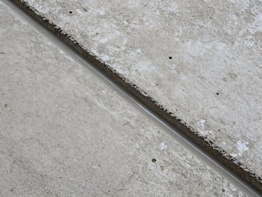 Tight close-up overhead shot of raw concrete substrate surface beside a freshly applied epoxy coating edge, showing the material transition zone, existing warehouse ambient light, no people, surface grain and pore detail clearly visible