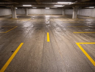 Wide overhead environmental shot of a parking level floor, epoxy with anti-slip aggregate and yellow lane markings, existing overhead lighting, no vehicles or people