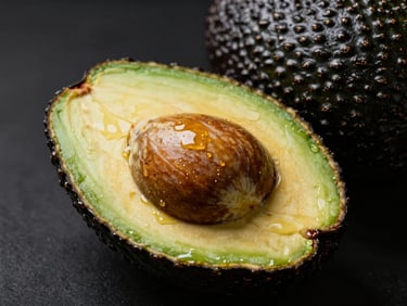 Perfect ripe avocado halved with pit, glistening flesh, dark moody background, studio lighting
