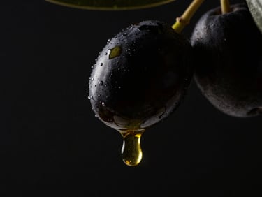 Macro close-up of a single glistening droplet of golden olive oil falling from a black olive, high-contrast spotlighting on a deep black backdrop, 8k.