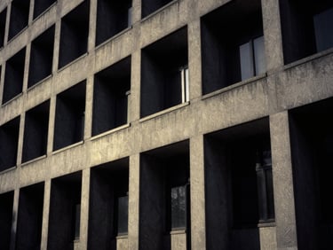 Stark black and white architectural photograph of a brutalist institutional facade, dramatic side-lighting, deep shadows, 35mm.