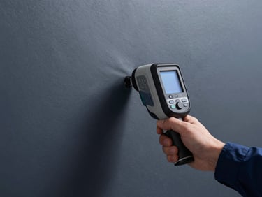 Thermal imaging camera view of a wall showing a hidden water leak, with an engineer's hand pointing, high-contrast cool daylight, deep navy and graphite tones, sharp focus, 35mm lens.