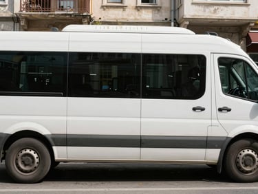 Side view of a white minibus parked on a sunny Istanbul street, large sliding door visible, clean exterior, ready for group transport