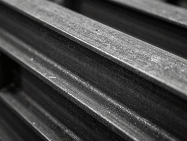 Extreme close-up of a raw, dark mill-finish steel beam, showing texture and subtle imperfections, harsh industrial lighting, black and white with mustard reflections, 35mm.