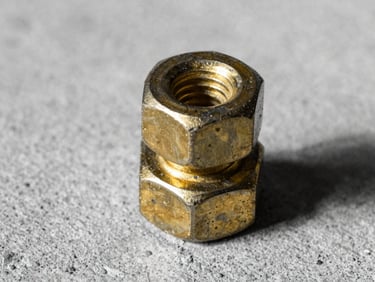 Close-up of a heavy-duty brass bolt and nut, geometric and textured, on a raw concrete surface, harsh light, black and white with mustard tint, 35mm.