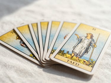 Close-up of gold-foiled tarot cards fanned out on a light linen cloth, soft shadows, sun-drenched, high-key lighting.