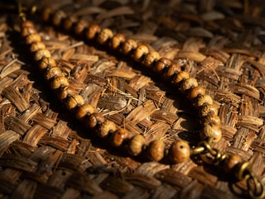 Macro photography of an Opele Ifá chain laid on a rustic woven straw mat, showing the textured details of the half-seeds and brass links under warm golden-hour side-lighting, deep shadows.