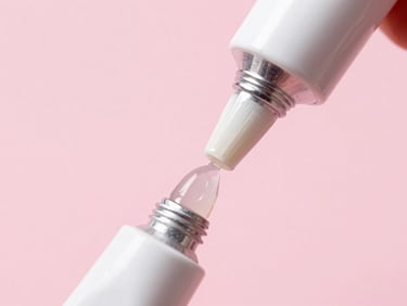 Close-up of a tube of solid gel glue being applied to a clear nail extension tip, bright pink background, studio lighting