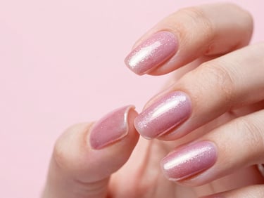 Macro shot of a manicured hand with shimmering pink chrome nails reflecting soft studio light, minimalist composition
