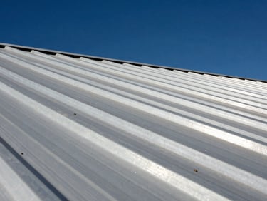 Low-angle shot of clean metal roof seams reflecting bright desert sun, structural metal lines against a deep blue sky.