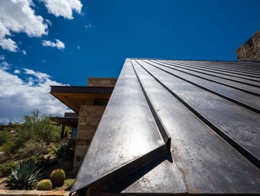 Low-angle architectural shot of a modern metal roof seam reflecting sharp desert sunlight under a deep blue Arizona sky.