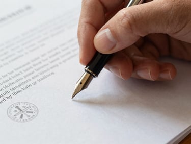 Close-up of a hand holding a fountain pen over a document with an official stamp, soft natural daylight, deep navy and warm paper tones, macro lens, shallow depth of field