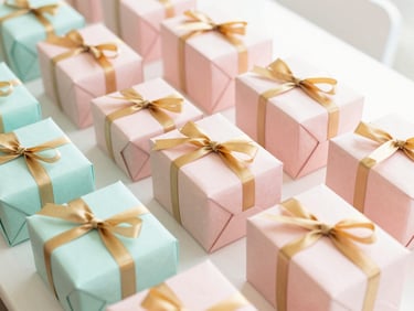 A bright creative workspace with organized stacks of blush pink gift boxes and warm gold ribbons for a large event, soft daylight