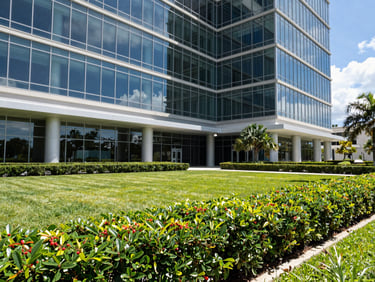 Wide-angle architectural photograph of a modern glass office building in Florida, featuring perfectly manicured hedges and immaculate green grounds.