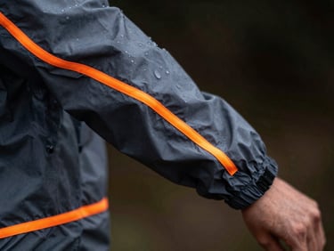 Macro shot of technical running windbreaker fabric with water droplets, reflective orange details, dark background