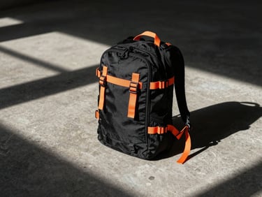 Technical black backpack with orange utility straps, concrete background, harsh sunlight shadows