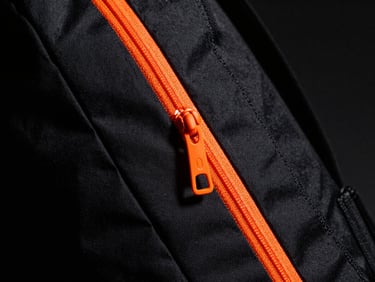 Macro shot of a black waterproof sports backpack with bright orange zippers, high contrast dramatic lighting, deep shadows