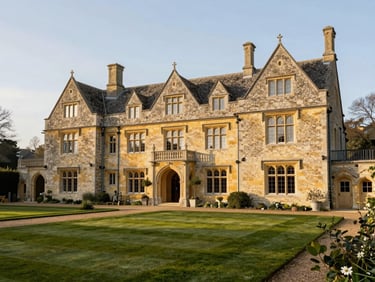 Architectural exterior of a grand Cotswold country estate at golden hour, manicured gardens, warm light, traditional stone.