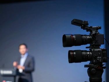 sharp corporate event photography, high-contrast stage lighting, professional camera capturing a speaker on stage with cool blue tones, shallow depth of field
