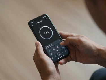 Overhead medium shot of hands holding an Android phone running a focus-duration training app, a clean elapsed-time ring visible on the dark screen, studio daylight, no background clutter