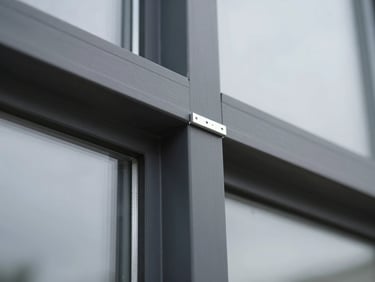 Close-up of a dark aluminum window frame corner seal on a building exterior, overcast daylight, precise installation detail, no people