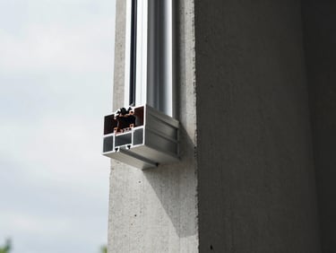 Close-up of an aluminum window frame corner joint on a building exterior, overcast daylight, precise miter seal visible, raw concrete wall surround, installation in progress