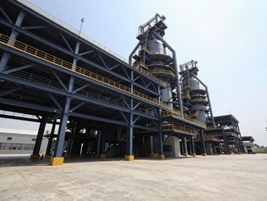 Low-angle architectural photograph of a massive modern industrial manufacturing facility in Gujarat, steel trusses, bright midday sun, concrete courtyard