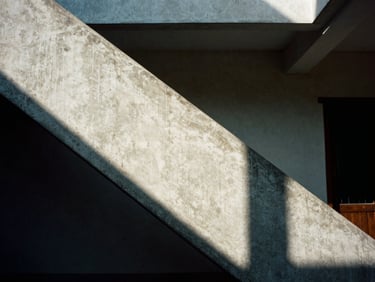 Cinematic close-up of geometric concrete staircase shadow in a modernist Vietnamese building, harsh sunlight creating sharp diagonal lines, deep shadows, 35mm film grain