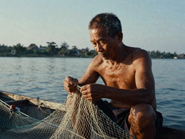 Cinematic portrait of an old Vietnamese fisherman repairing his net in quiet morning light, high-contrast natural light, deep shadows, highly textured skin, 35mm film grain
