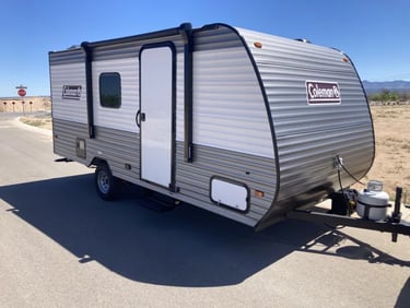 A gray and white Coleman Lantern travel trailer parked on a road for a camping trip.
