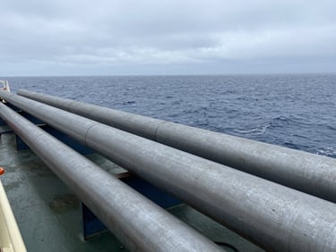 Close-up of a heavy industrial pipe-laying vessel deck with steel pipes, overcast North Sea light.