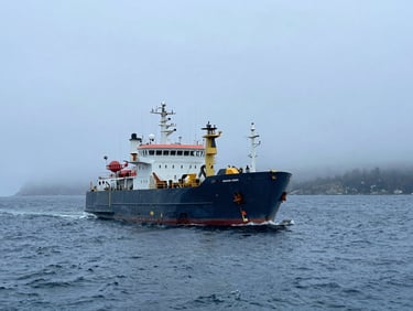 Offshore construction vessel operating in cold waters, misty Canadian coastline background.
