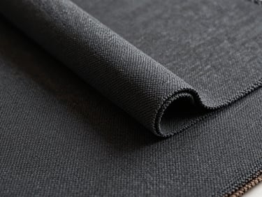 Close-up flat-lay of heavyweight contract upholstery fabric swatch in deep charcoal, tight weave pattern visible under soft diffused daylight, fabric edge slightly rolled to show pile depth