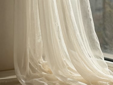 Close-up of a sheer voile fabric swatch in ivory, delicate open weave caught in soft north-facing window light, fabric draped gently to show translucency and fine texture