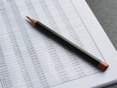 Overhead shot of a printed data table with statistical annotations, a pencil resting across rows, cool overhead institutional lighting, clean white surface