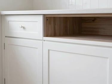 A kitchen cabinet, half refinished in a pristine white, half still in its original dark wood, demonstrating a flawless transformation. Close-up, natural coastal daylight.